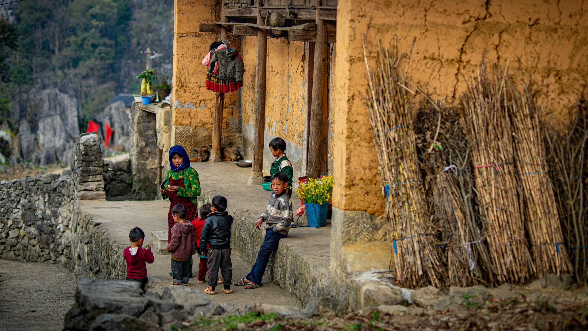 Enfants des minorités ethniques jouant devant une maison traditionnelle en terre battue à Ha Giang