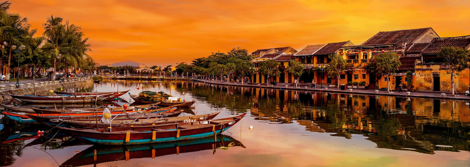 Barques traditionnelles sur la rivière Hoai à Hoi An au coucher du soleil avec des maisons anciennes jaunes