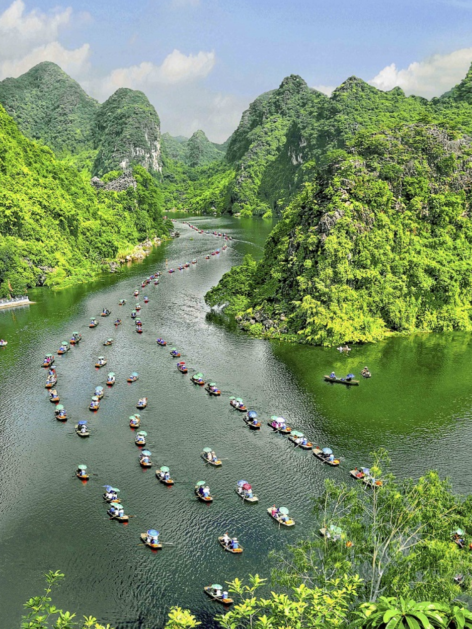 Longue file de barques traditionnelles transportant des touristes à travers le paysage karstique spectaculaire de Ninh Binh