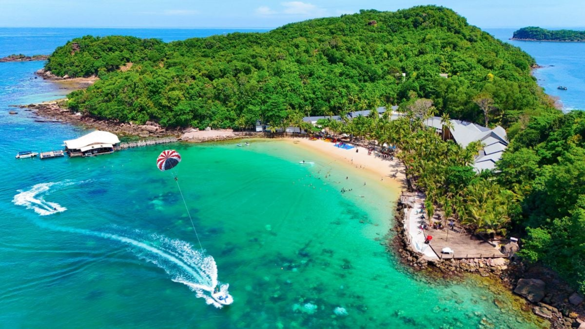 Parachute ascensionnel et activités nautiques sur une plage de sable blanc bordée de palmiers à Phu Quoc