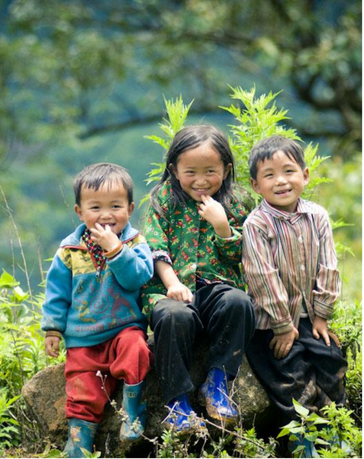 Trois enfants montagnards souriants assis sur un rocher au milieu d'une végétation luxuriante